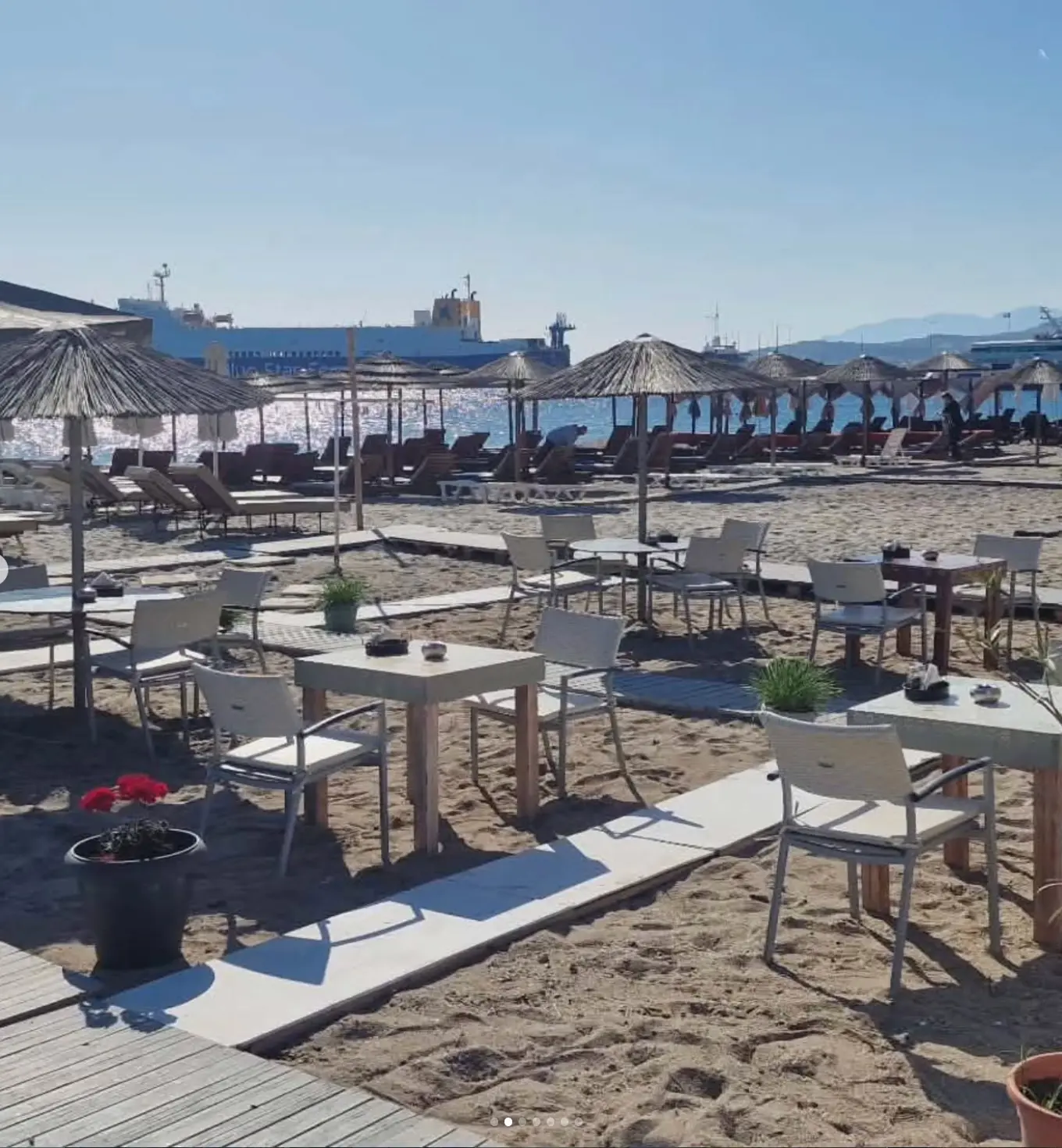 Tables and straw parasols set out on the sand in front of the taverna